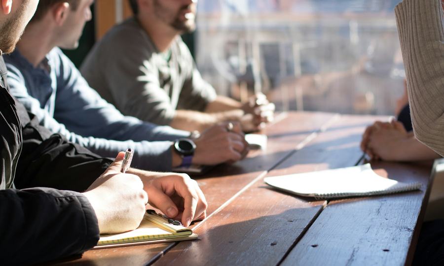 Equipo reunido alrededor de una mesa de trabajo tomando notas en cuadernos